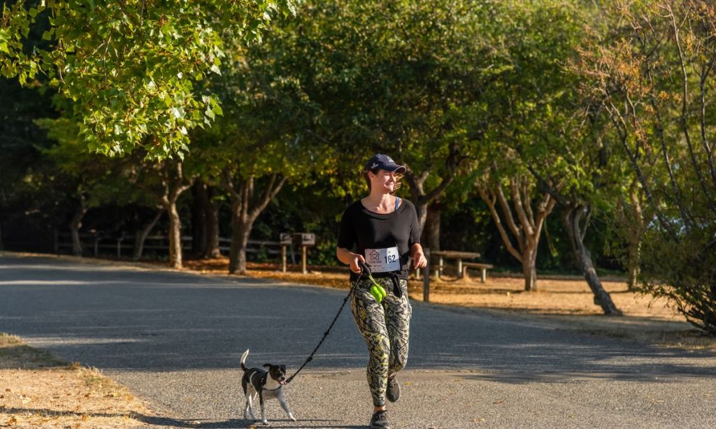 Woman jogging on a park path with her leashed dog in natural daylight